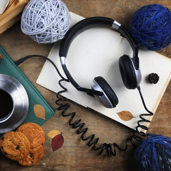 Et par høretelefoner ligger på et bord med kaffe og garnnøgler